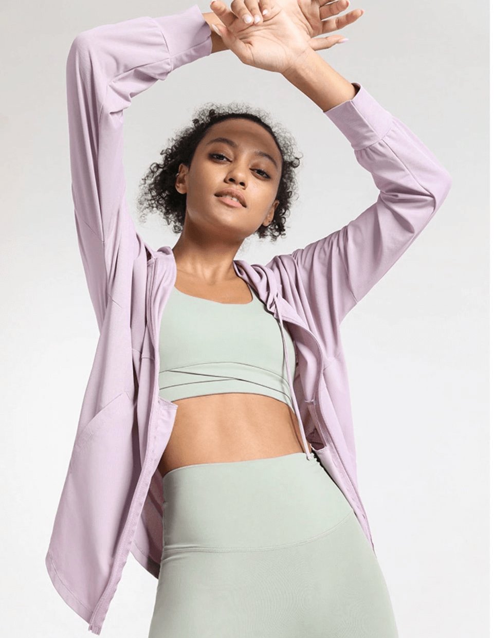 Woman wearing a loose-fitting lavender sports jacket with hood, ideal for running, jogging, and yoga. Flexible, breathable design.